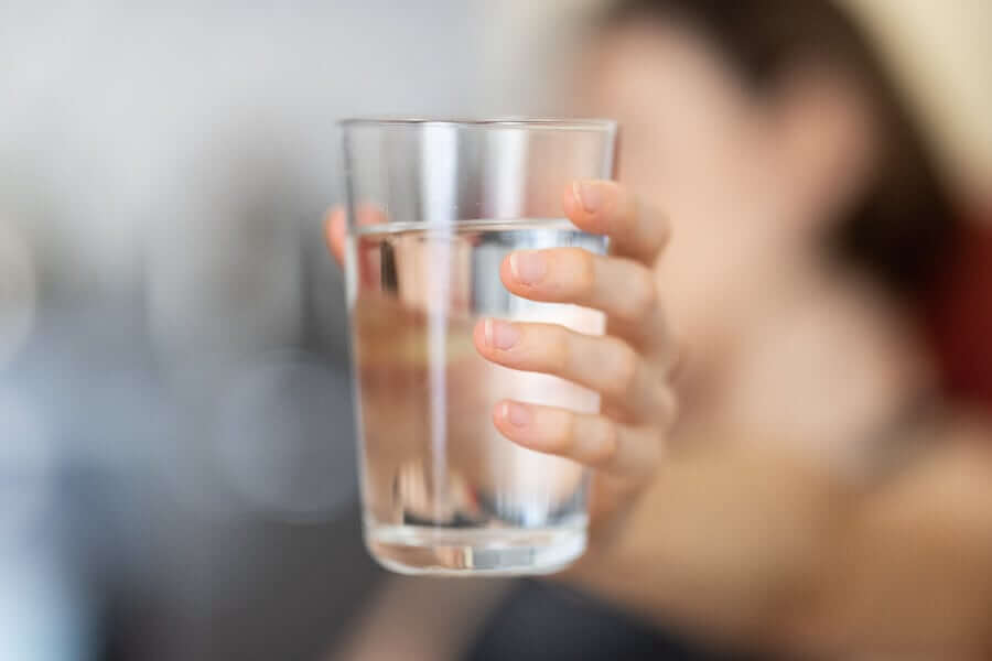 A hand holding a glass of water with a blurred background.