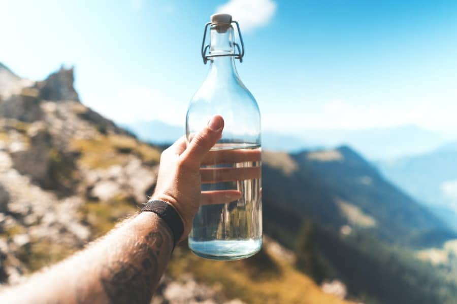 Clear Glass Bottle of Water Being Held Up in Front of Mountians